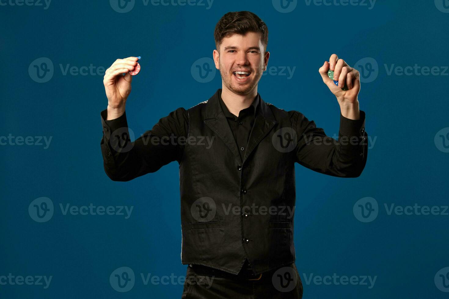 novizio nel poker, nel nero veste e camicia. Tenere alcuni colorato patatine fritte. in posa contro blu sfondo. gioco d'azzardo, casinò. avvicinamento. foto