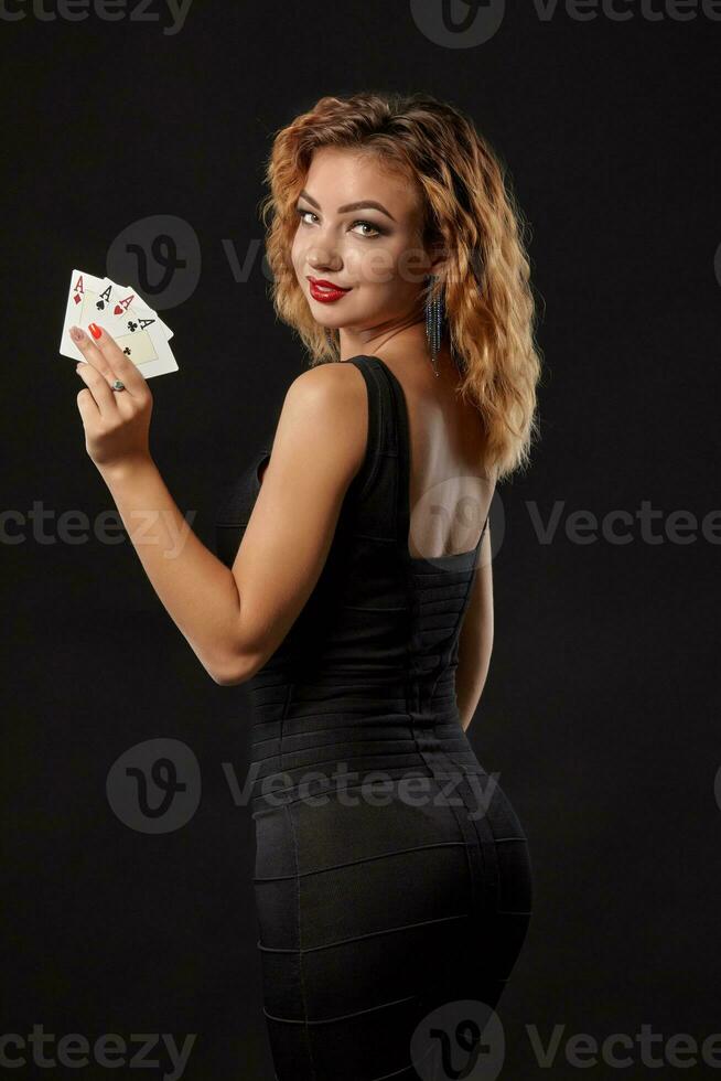 Zenzero ragazza indossare un' buio vestito è in posa Tenere quattro assi nel sua mani in piedi contro un' nero studio sfondo. casinò, poker. avvicinamento. foto