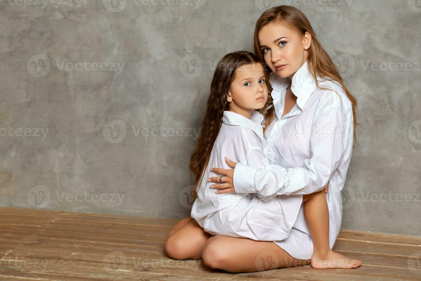 interno ritratto di un' bellissimo madre con sua affascinante poco figlia in posa contro un' grigio parete. foto