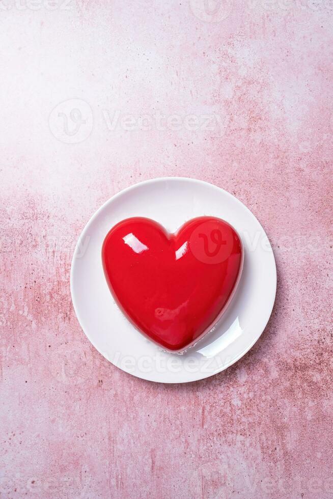 cuore sagomato smaltato San Valentino torta su bianca piatto su rosa calcestruzzo sfondo foto