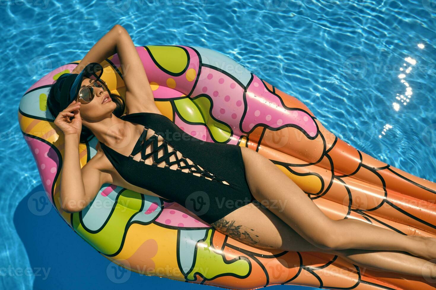 ritratto di un' femmina avendo riposo e in posa nel un' nuoto piscina su un gonfiabile materasso. vestito nel un' nero costume da bagno, parasole berretto e occhiali da sole. foto