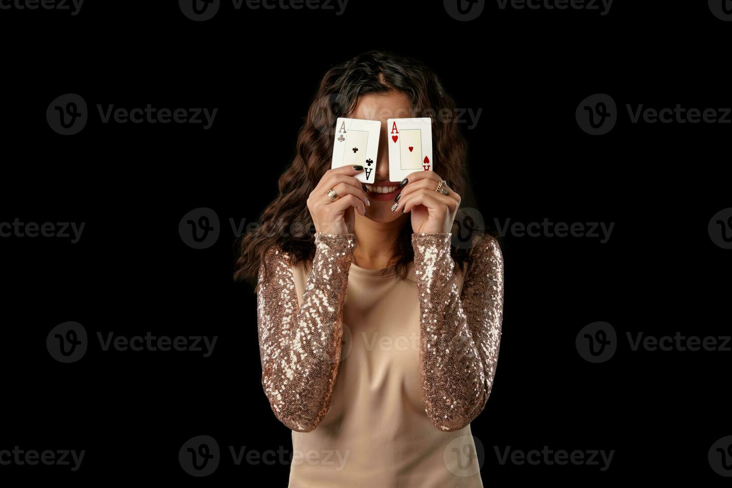 brunetta ragazza indossare brillante vestito in posa Tenere Due giocando carte nel sua mani in piedi contro nero studio sfondo. casinò, poker. avvicinamento. foto