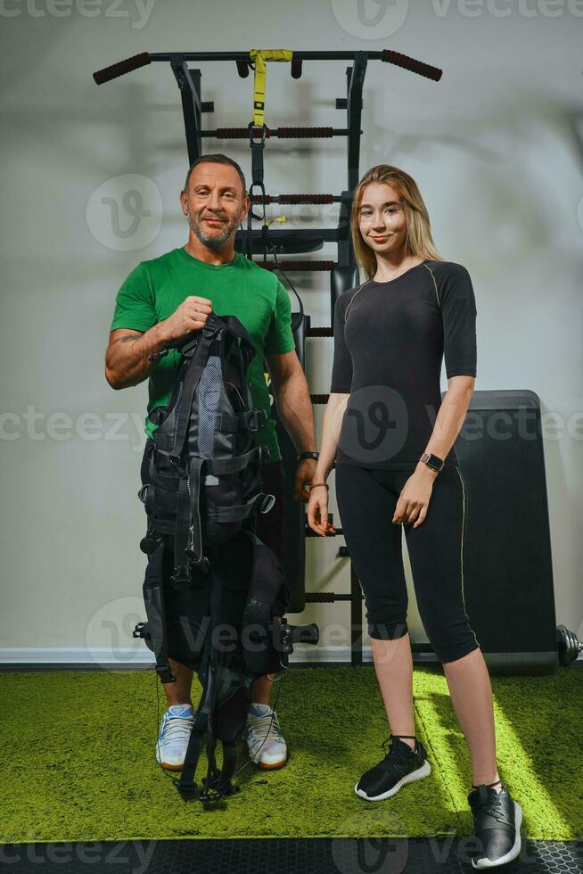 muscolare fitness istruttore è mettendo su un ems completo da uomo per atletico donna. formazione nel un' Palestra di un' metodo per aumentare energia. foto