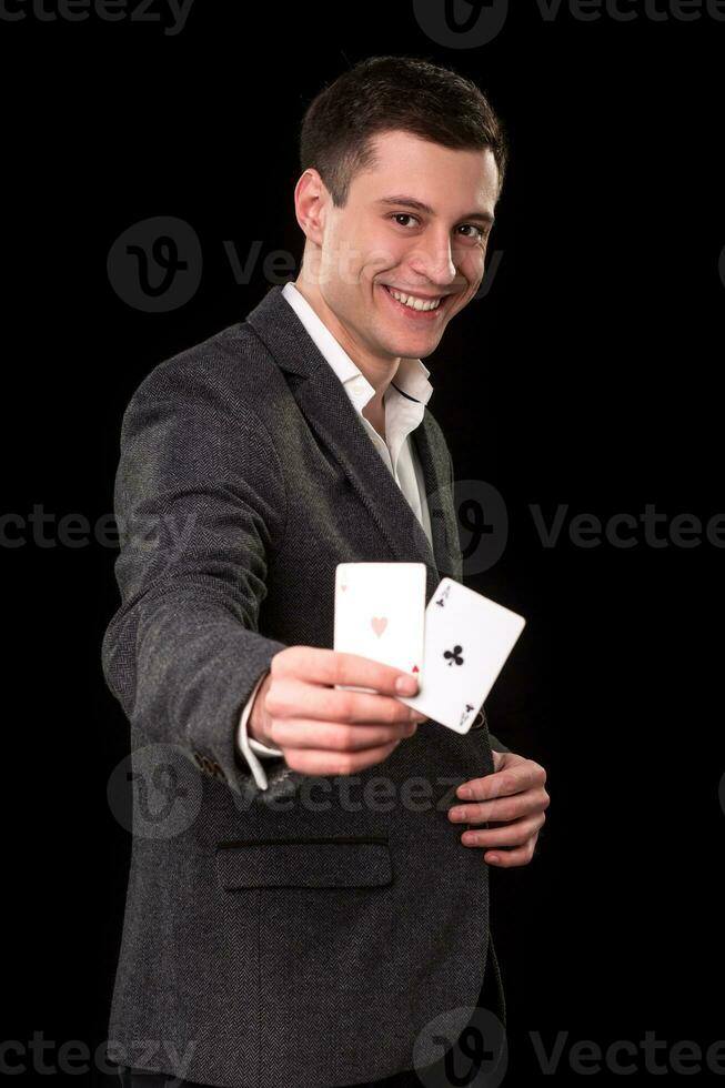 giovane caucasico uomo indossare completo da uomo Tenere Due assi nel il suo mano su nero sfondo. gioco d'azzardo concetto. casinò foto