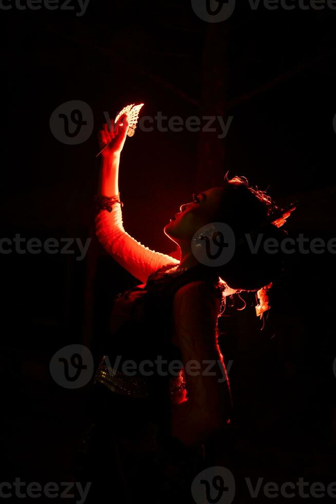 silhouette di un' femmina ballerino Tenere gioielleria nel il mezzo di il immobilità di il notte con rosso leggero foto