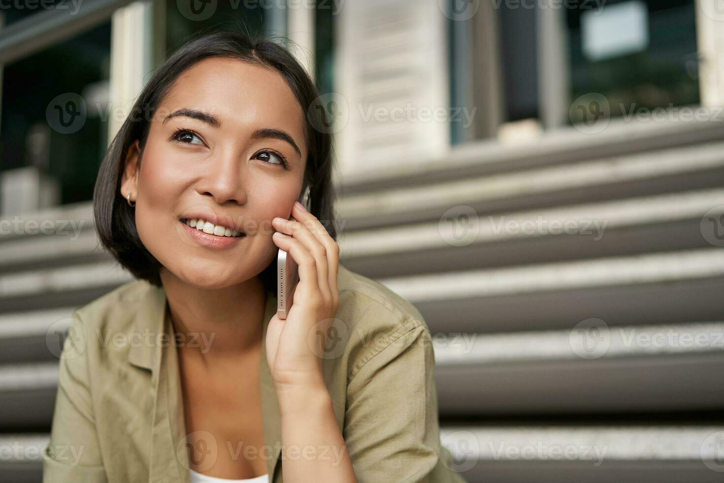 cellulare tecnologia. sorridente asiatico ragazza parla su mobile Telefono, fa un' chiamata. giovane donna con telefono si siede su le scale foto