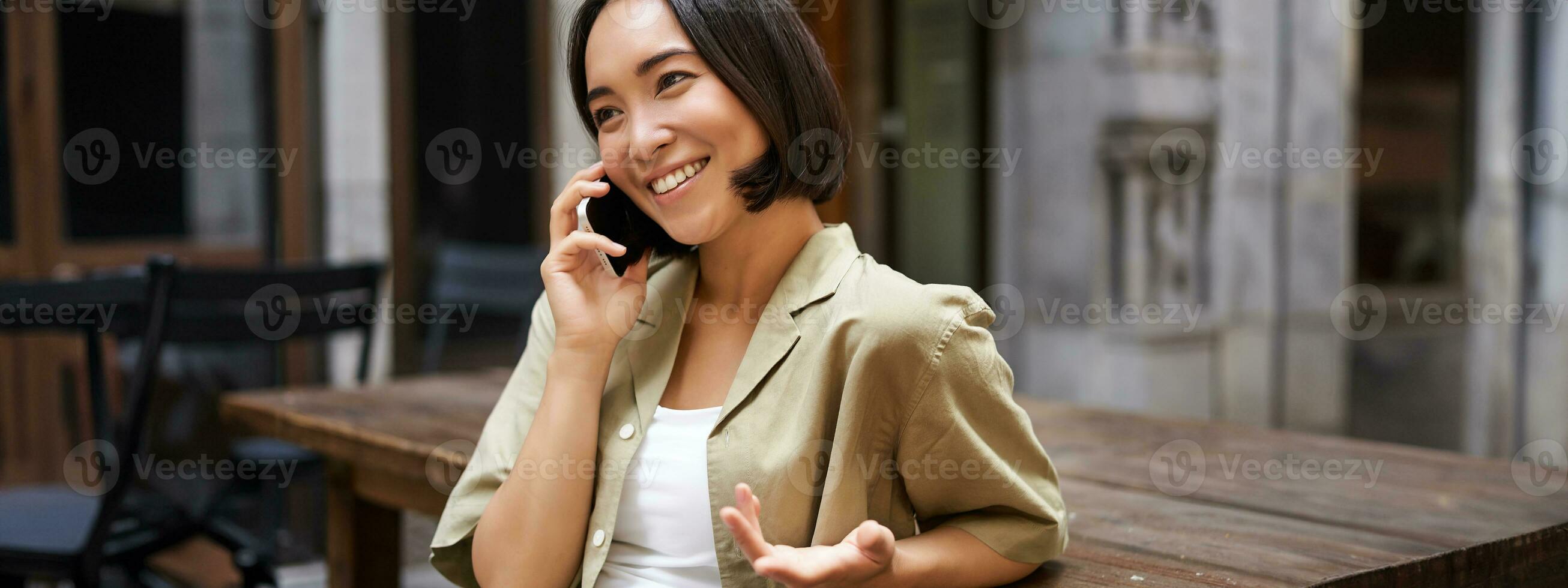 giovane donna avendo conversazione su mobile Telefono, seduta all'aperto e fabbricazione Telefono chiamata, utilizzando smartphone, parlando foto
