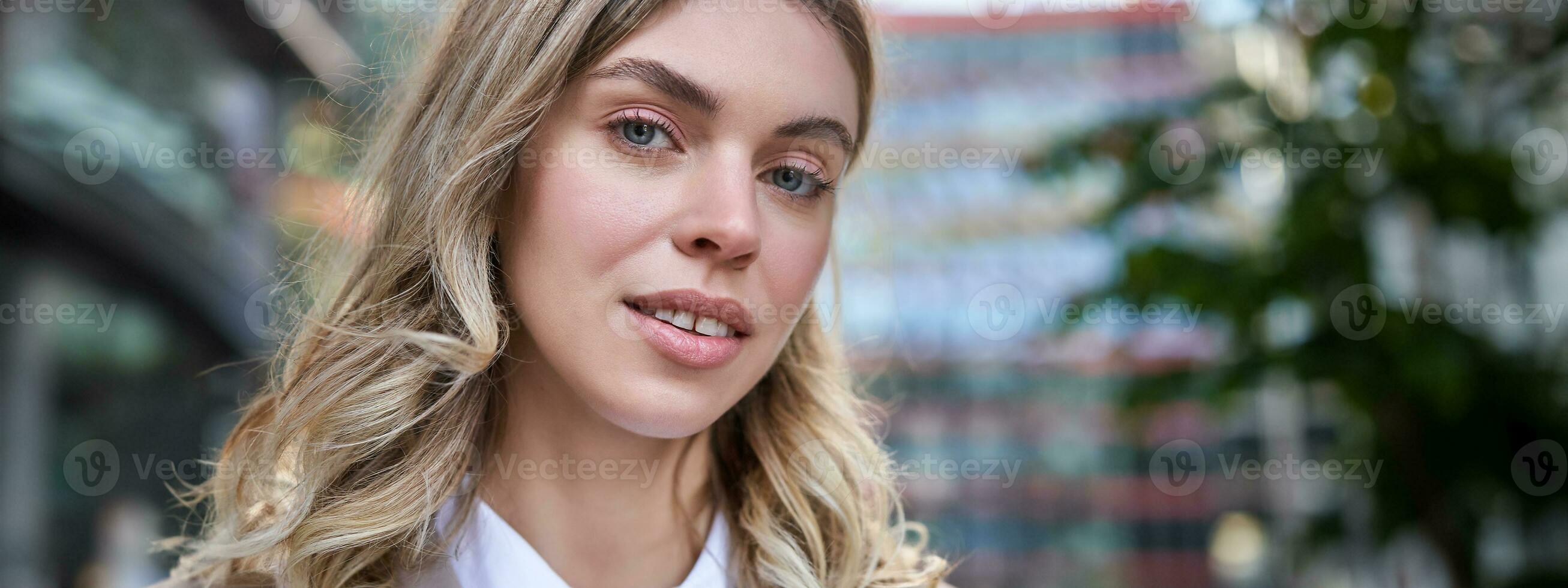 vicino su ritratto di sorridente, bellissimo donna 25 anni vecchio, indossare aziendale vestiario, guardare felice, in piedi al di fuori su strada foto