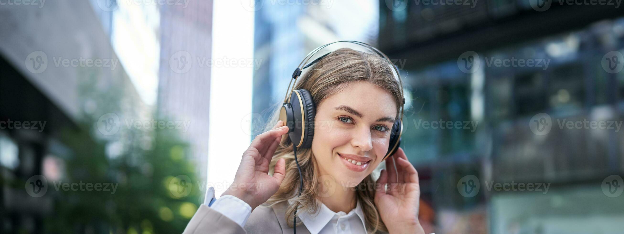 contento donna ascolta per musica nel cuffie mentre a piedi nel città centro, sorridente foto