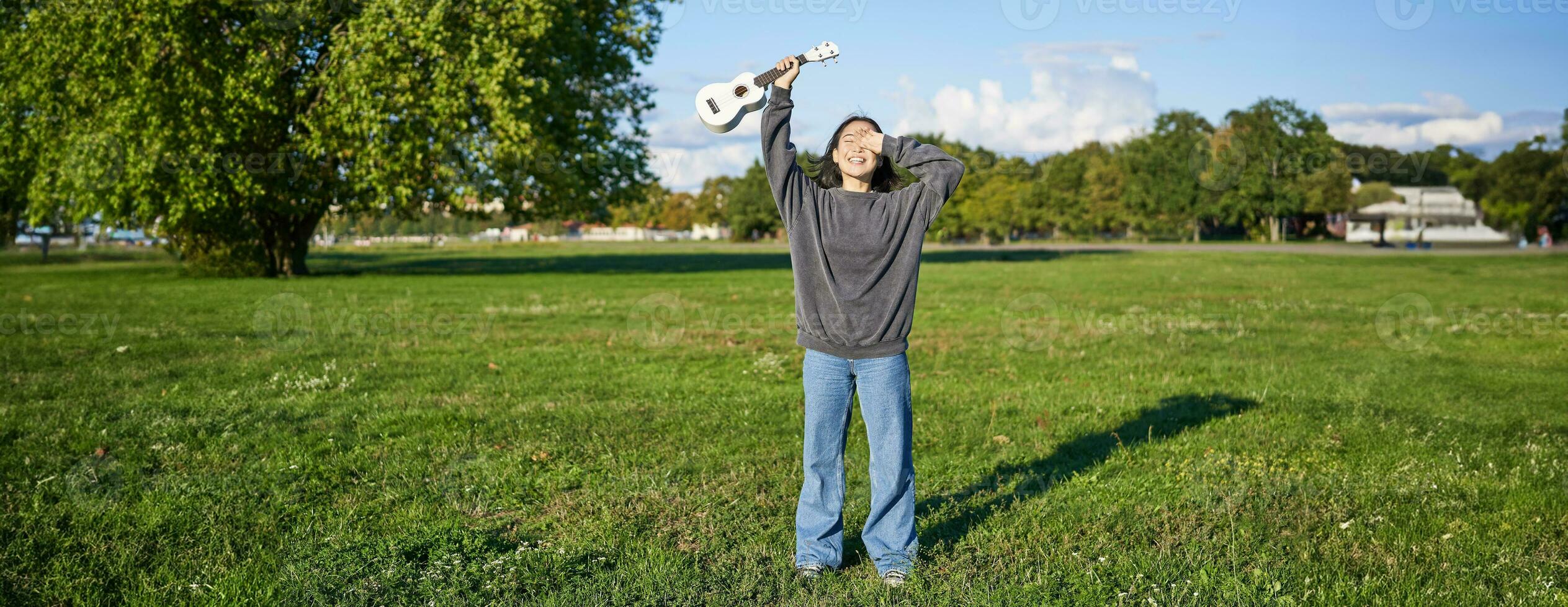 contento asiatico ragazza, musicista con ukulele, sensazione spensierato, godendo la libertà e fresco aria all'aperto, giocando musicale strumento foto