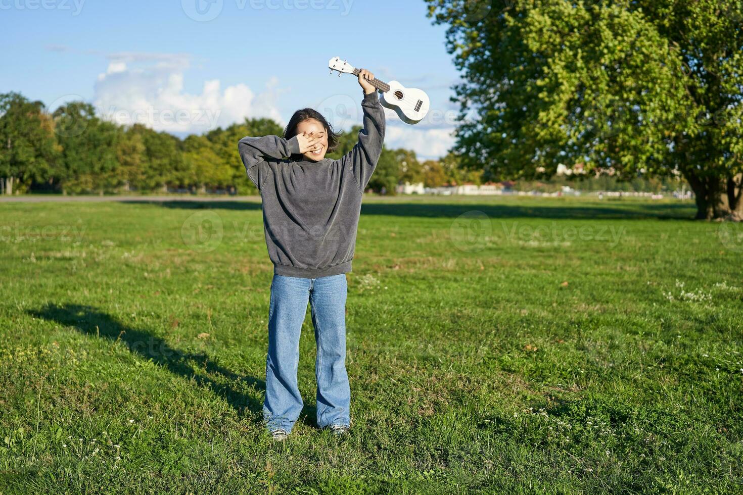 contento asiatico ragazza, musicista con ukulele, sensazione spensierato, godendo la libertà e fresco aria all'aperto, giocando musicale strumento foto