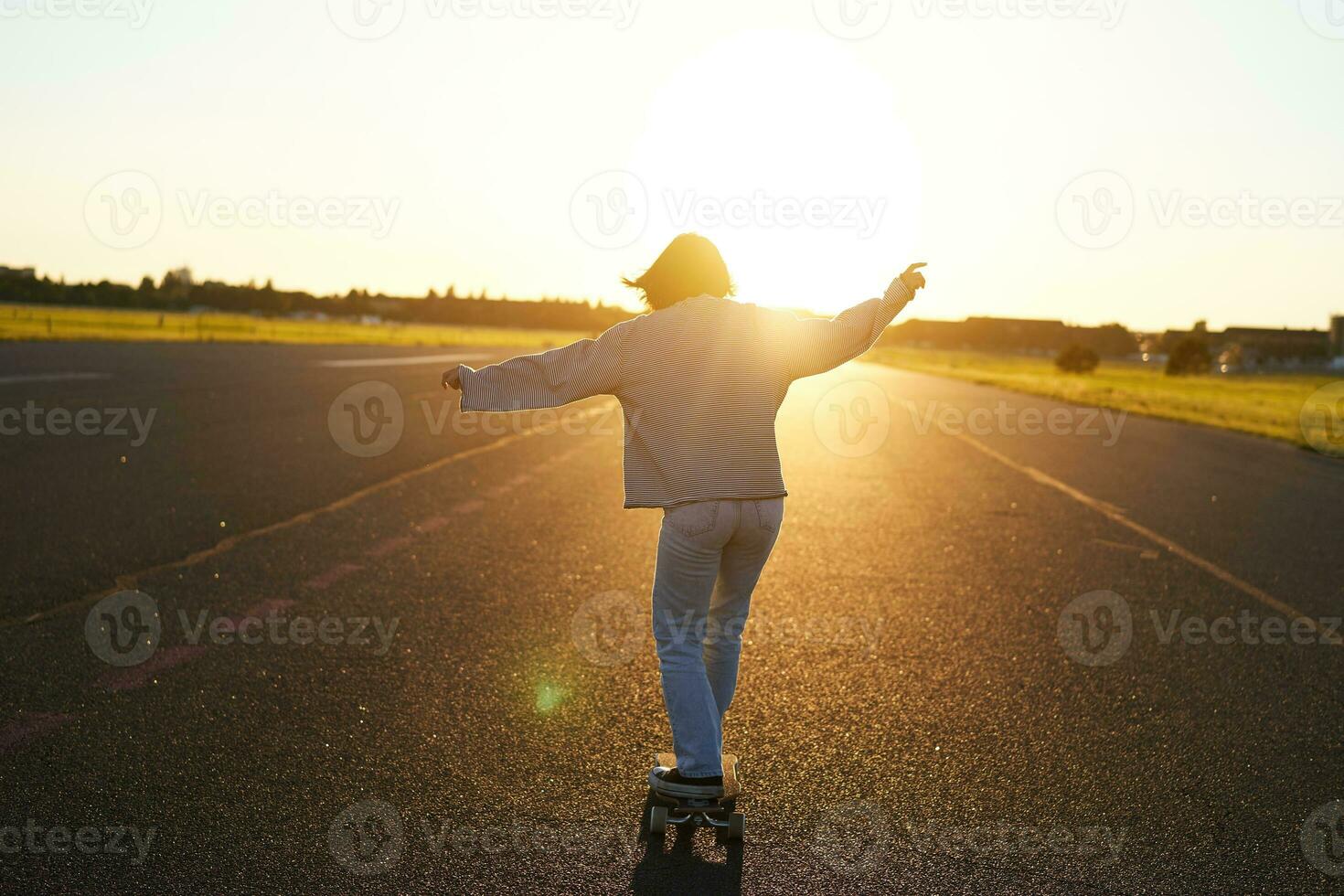 adolescente ragazza sensazione contento su longboard. contento giovane pattinatore equitazione sua skateboard con mani diffusione di lato, sensazione libertà, andando in direzione il sole foto