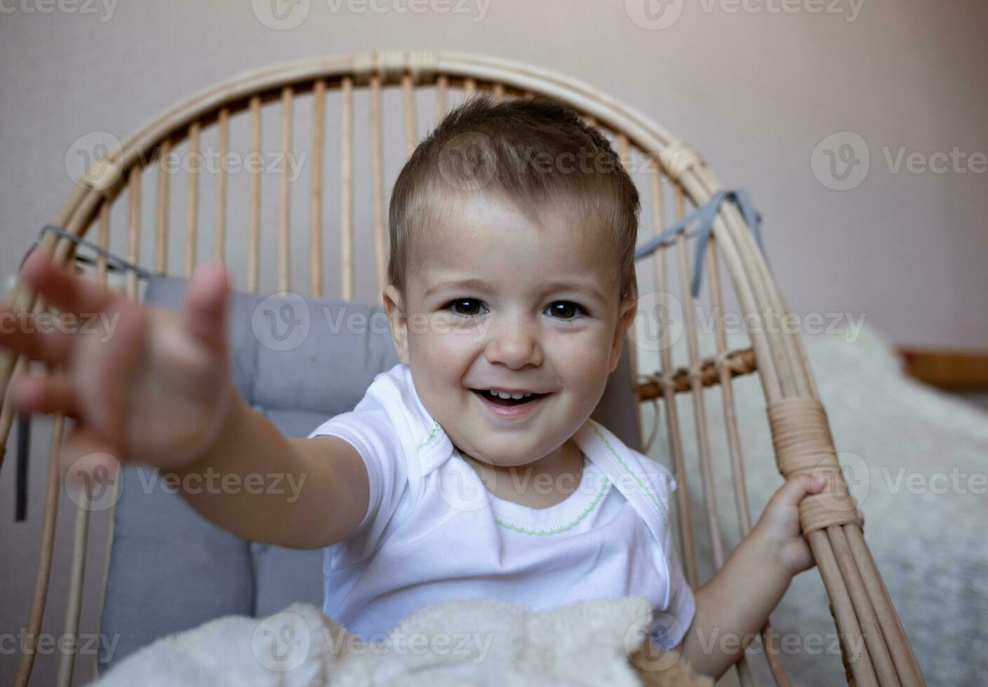 poco carino ragazzo sorridente mentre seduta nel un' sedia nel il Camera da letto foto