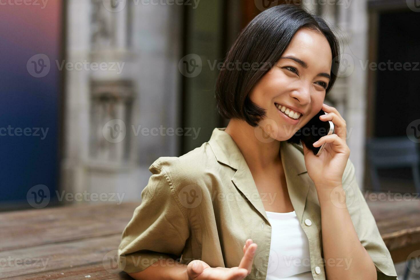 giovane donna avendo conversazione su mobile Telefono, seduta all'aperto e fabbricazione Telefono chiamata, utilizzando smartphone, parlando foto