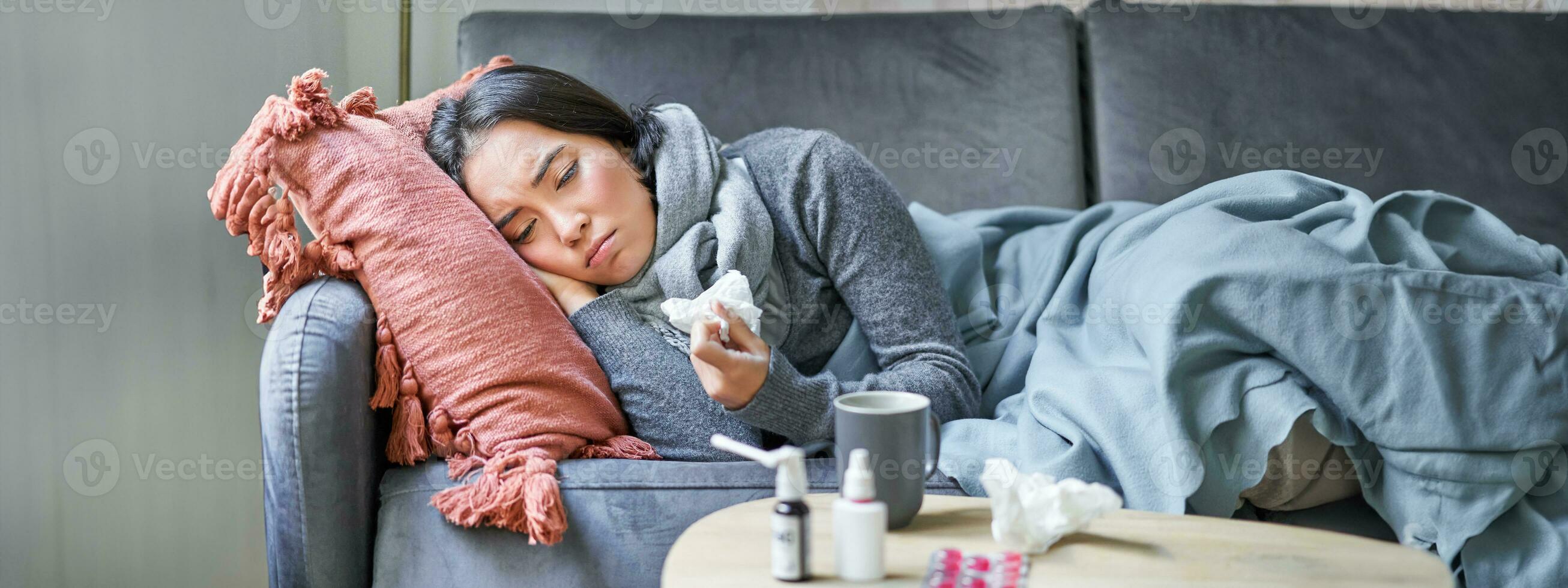 malato triste coreano donna dire bugie su divano, sensazione male, attraente freddo, influenza e temperatura, guardare rovesciato, assunzione medicazione foto