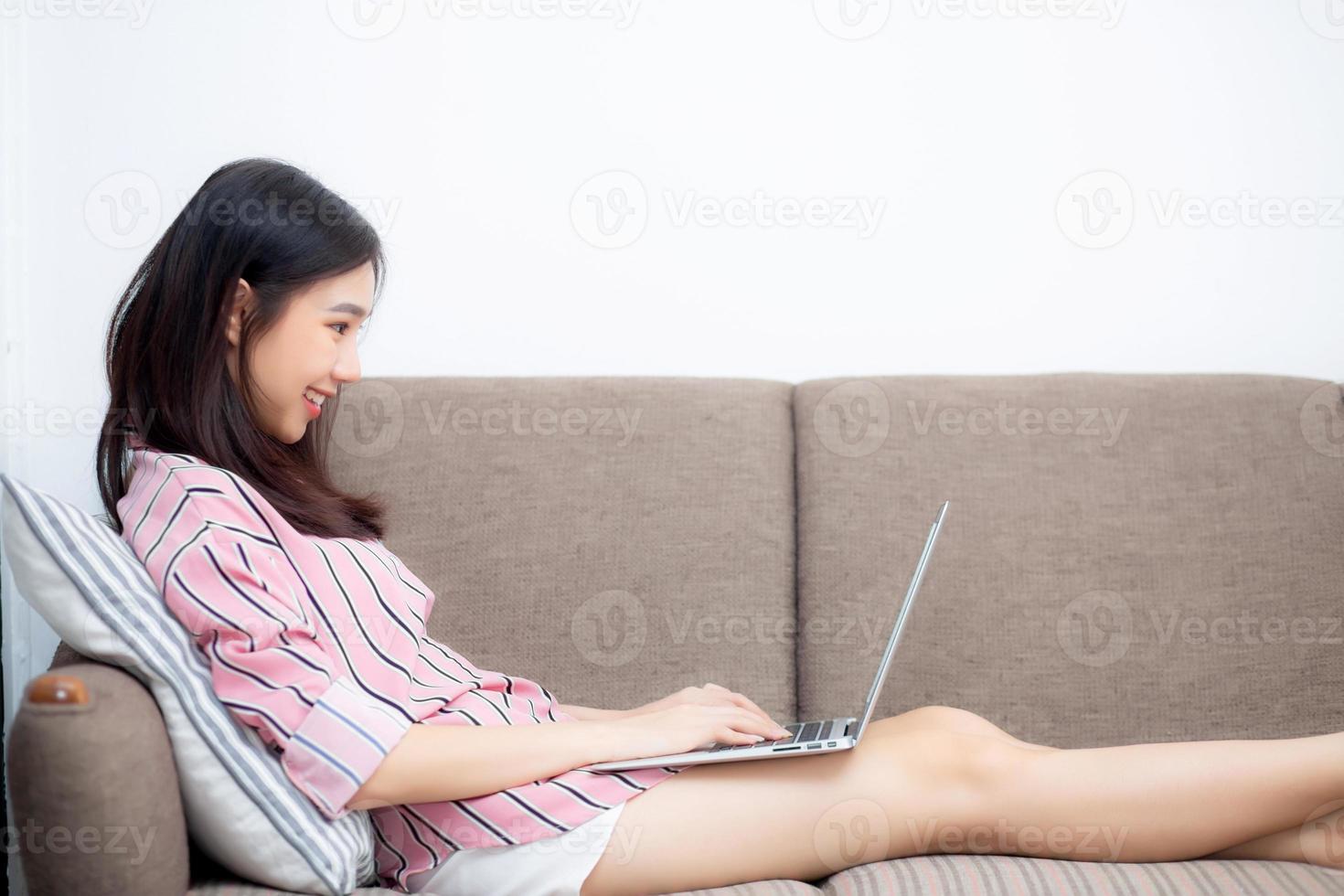 giovane donna asiatica che lavora al computer portatile e che si siede sul divano. foto