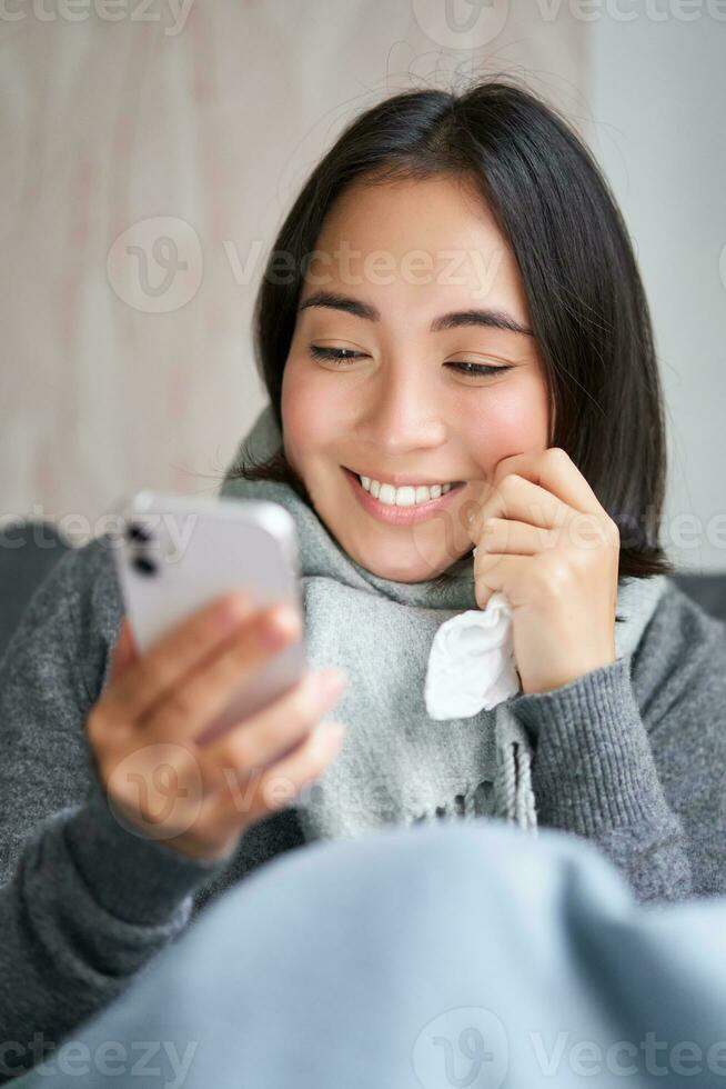 ritratto di coreano donna si sente malato, Tenere smartphone, chiamata medico gp per ottenere prescrizione, catturato freddo, soggiorno a casa, utilizzando mobile Telefono foto