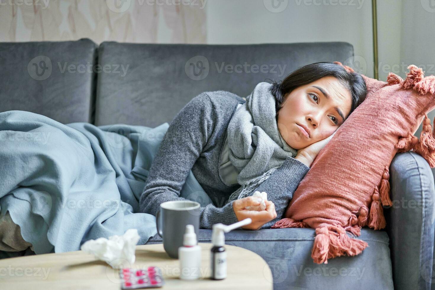 malato triste coreano donna dire bugie su divano, sensazione male, attraente freddo, influenza e temperatura, guardare rovesciato, assunzione medicazione foto