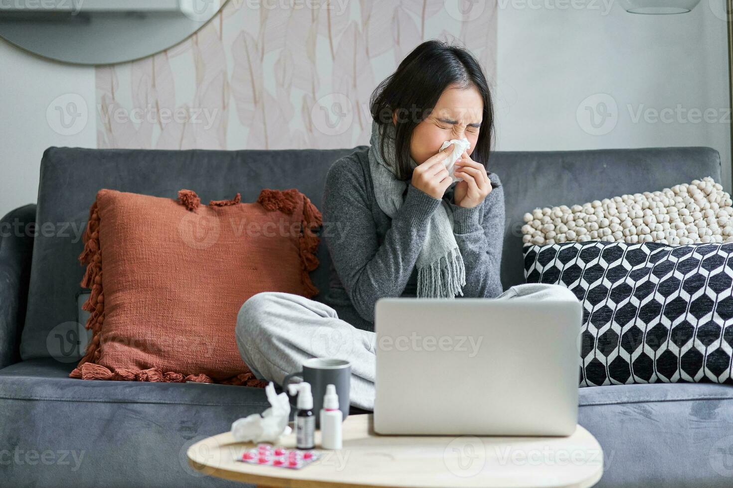 giovane asiatico donna soggiorno a casa, sensazione male, attraente un' freddo, malato partire, seduta con computer portatile, Guardando film su computer, starnuti foto