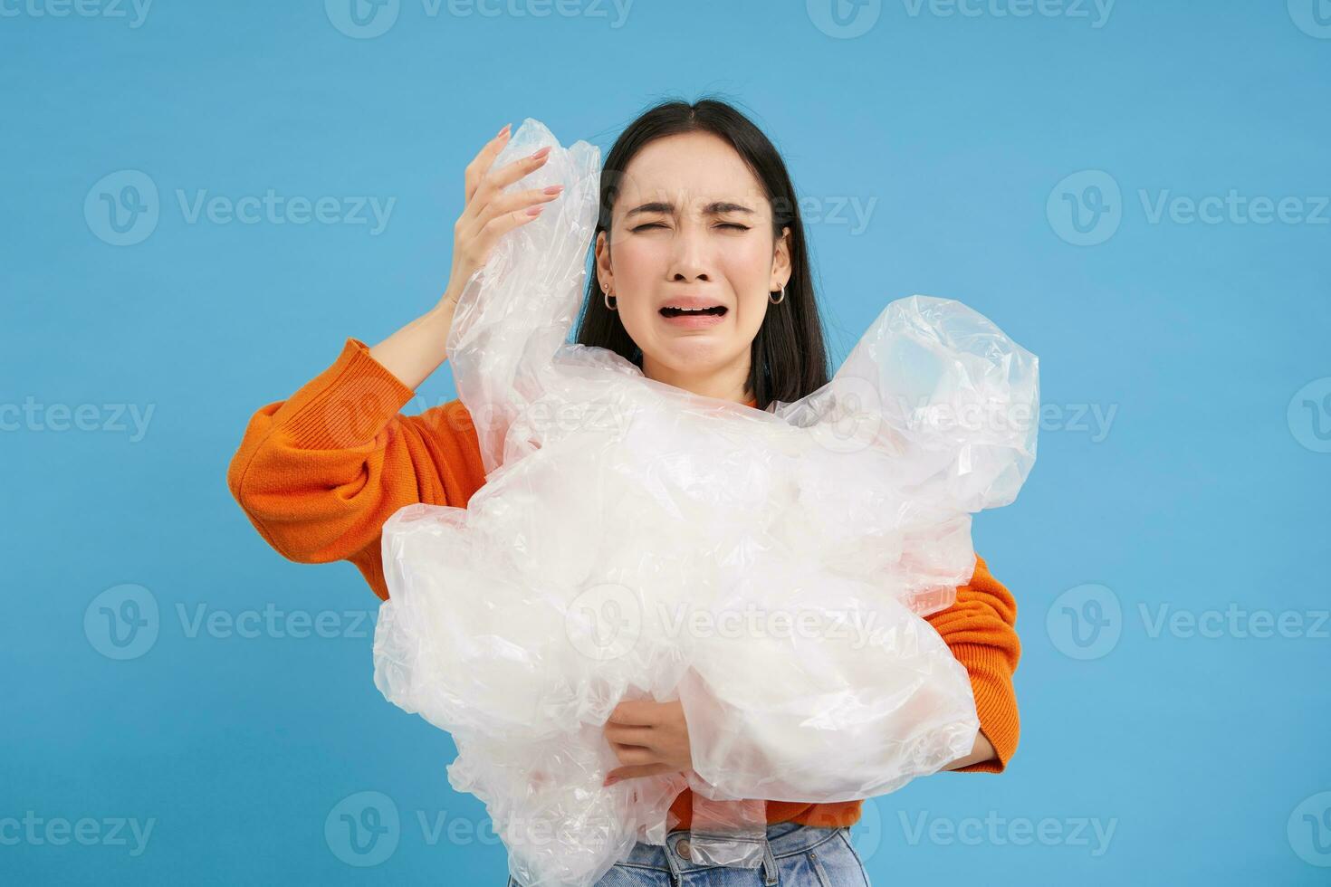 pianto asiatico donna con plastica raccolta differenziata sciupare, stanco di ordinamento spazzatura in diverso bidoni, preservare natura, blu sfondo foto