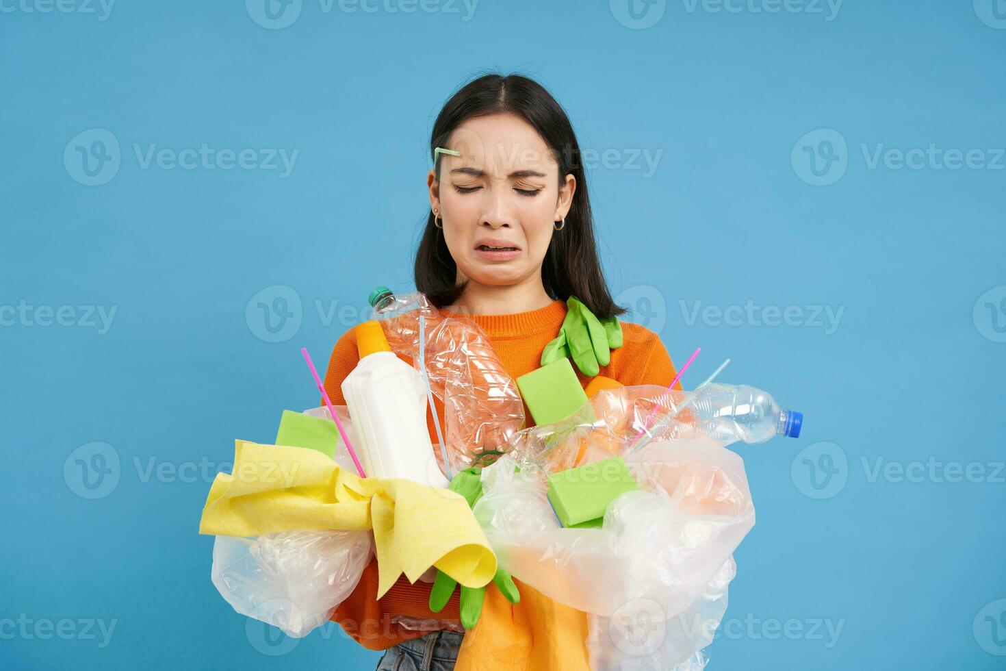 triste asiatico femmina alunno, detiene raccolta differenziata sciupare, raccoglie plastica spazzatura per prendere esso per riciclare centro, blu sfondo foto