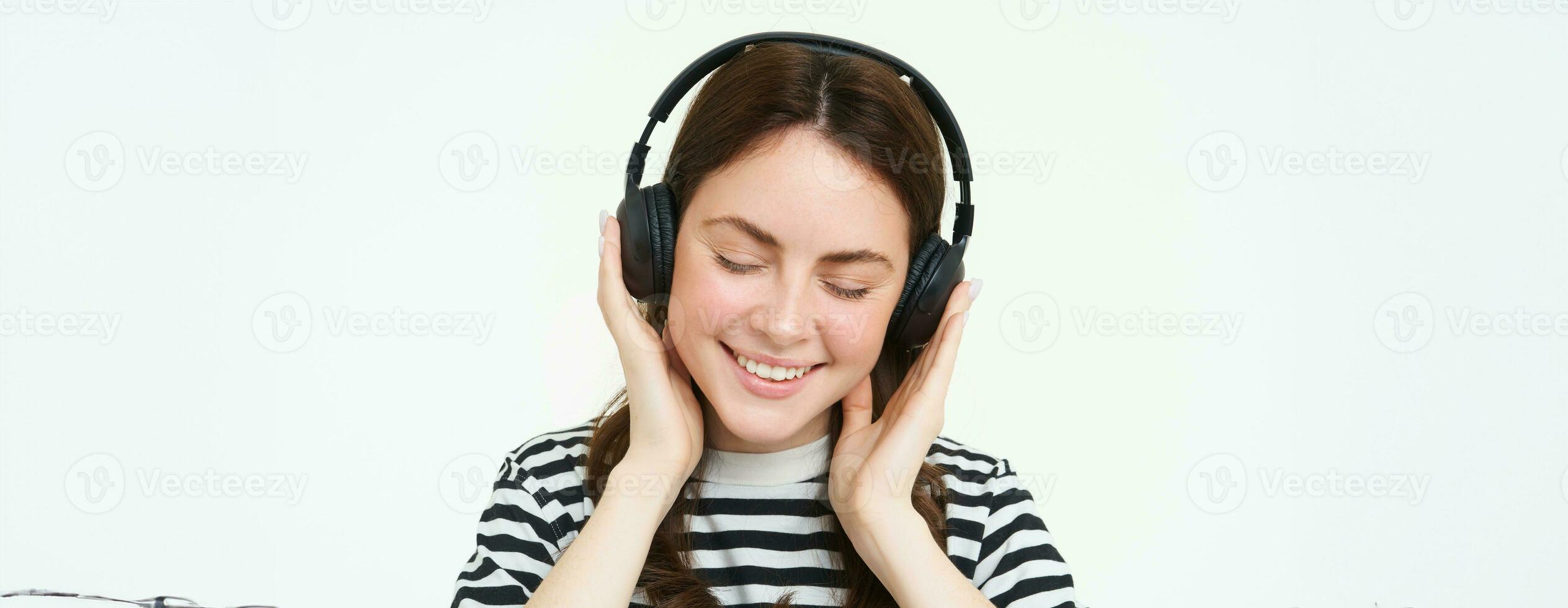 ritratto di donna, sorridente, indossare senza fili cuffia, ascoltando musica, studiando nel auricolari, in piedi isolato al di sopra di bianca sfondo foto