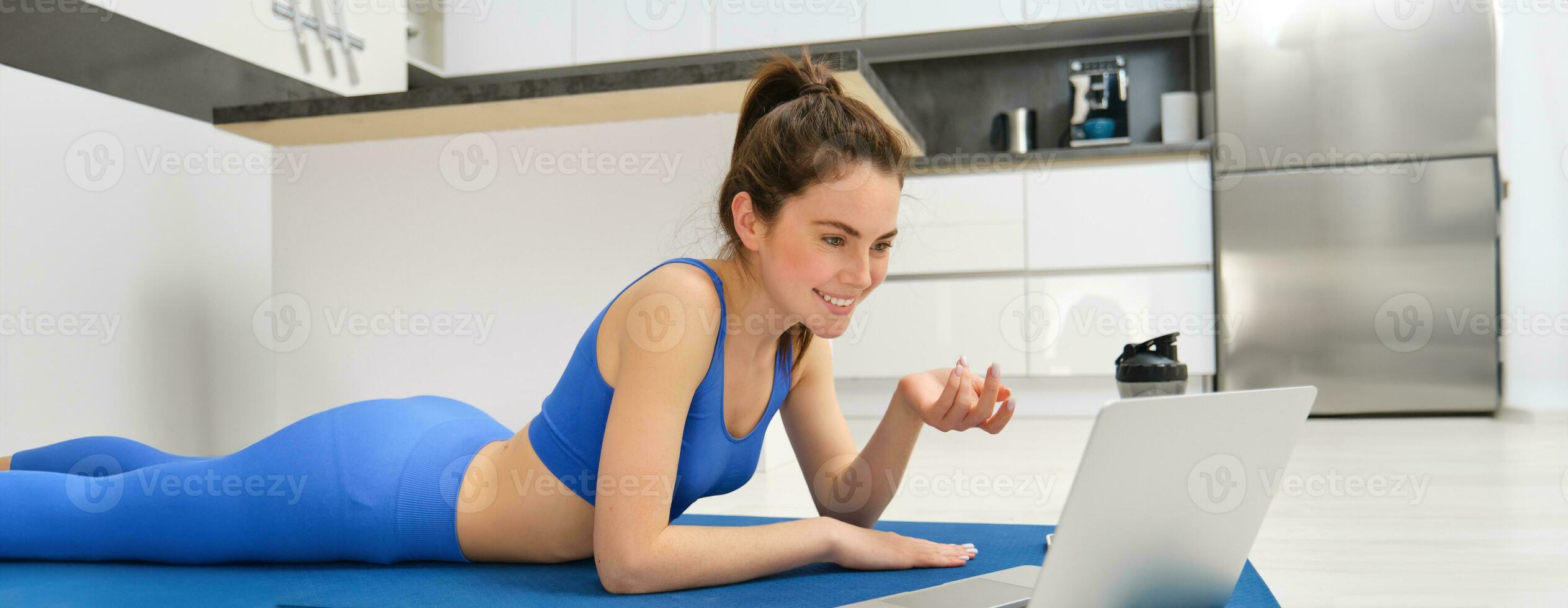 Immagine di giovane fitness ragazza parlando in linea su computer portatile, video chat, posa su pavimento gomma da cancellare stuoia, fare esercizi, discutere allenarsi addestramento, yoga a partire dal casa foto