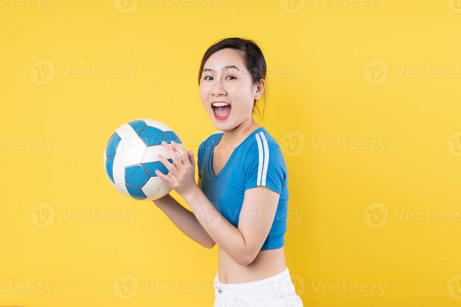 Ritratto di giovane ragazza dinamica che tiene la palla in mano isolata su sfondo giallo foto