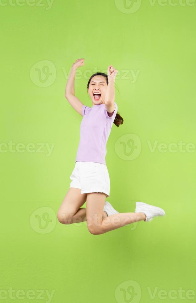 corpo pieno giovane ragazza asiatica che salta, isolato su sfondo verde foto