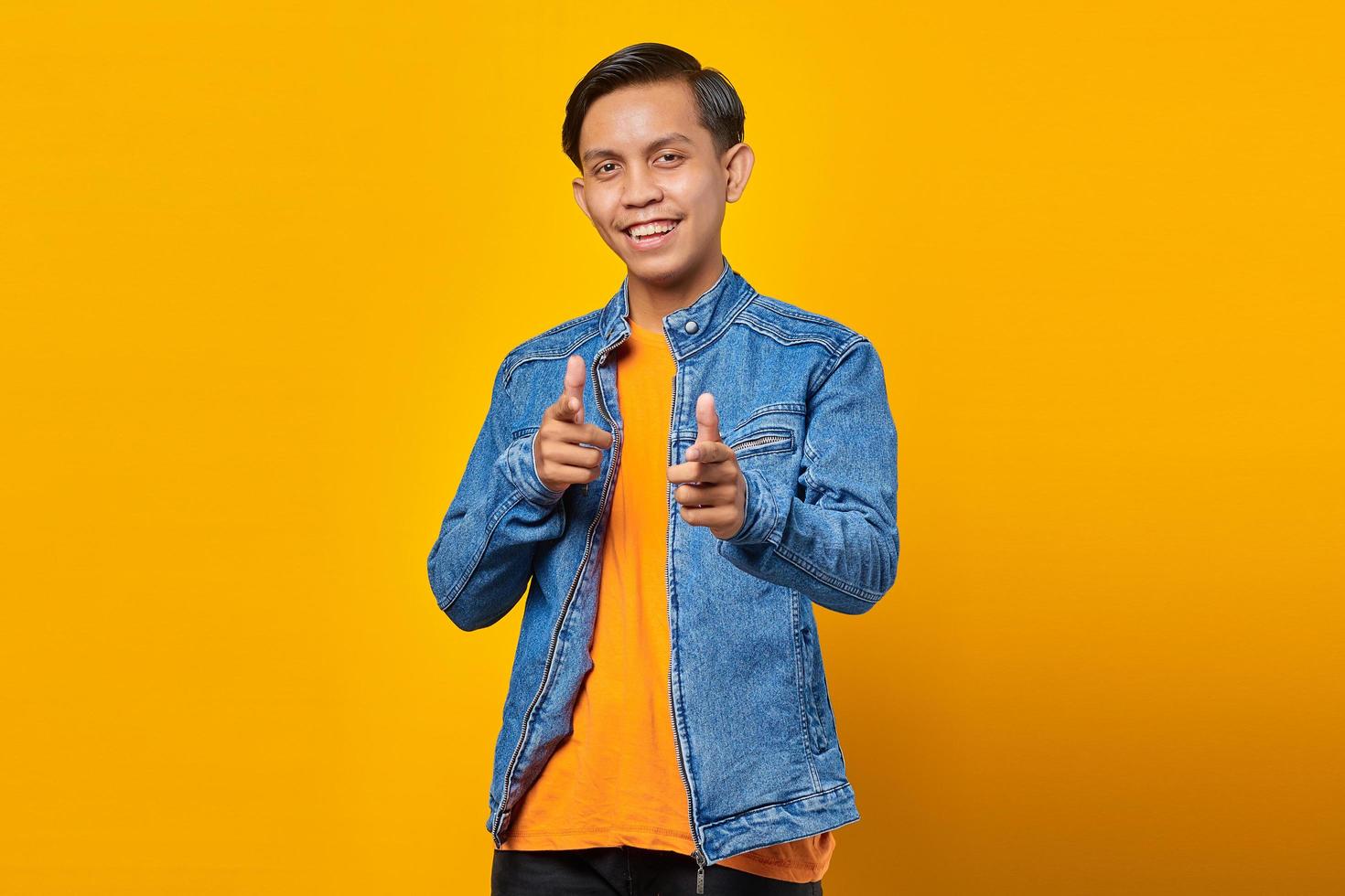 ritratto di giovane uomo asiatico sorridente che punta alla telecamera con due dita isolate su sfondo giallo foto