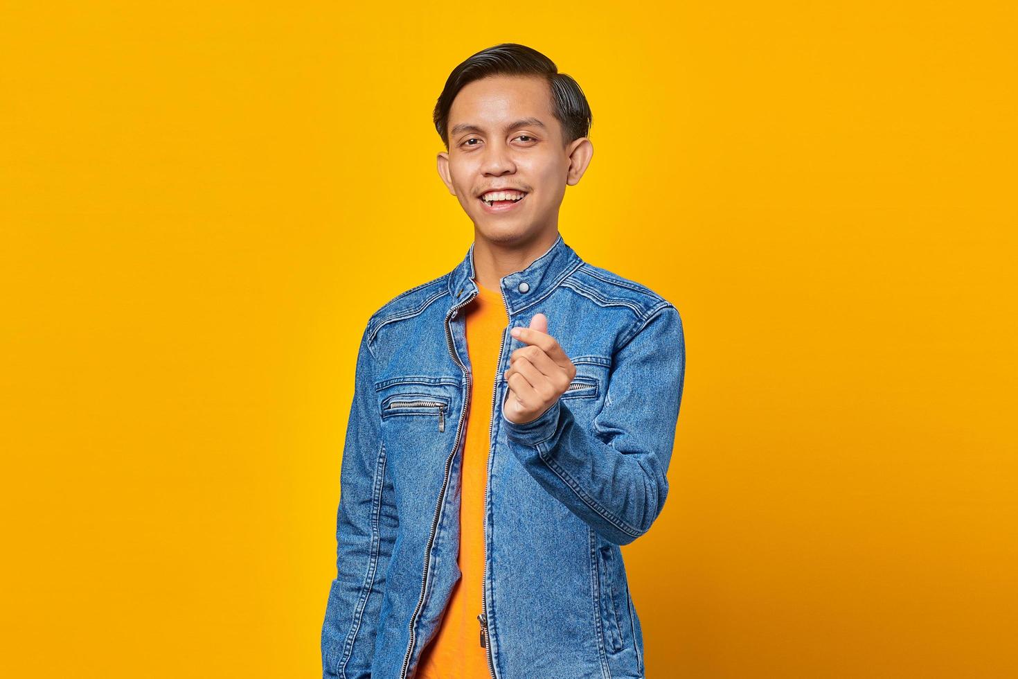 ritratto di giovane uomo asiatico sorridente che mostra il cuore del dito su sfondo giallo foto