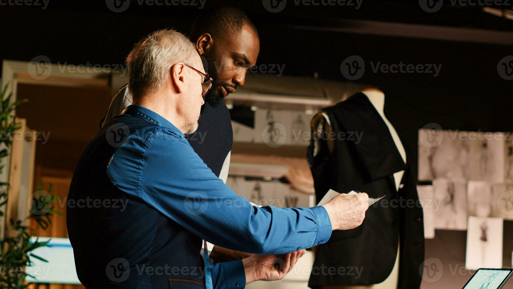 couturier e allievo controllo schizzi nel sarto officina, apprendimento per mestiere capi di abbigliamento linea fatto a mano. moda progettista e apprendista discutere di Modelli e tessuto. palmare sparo. foto