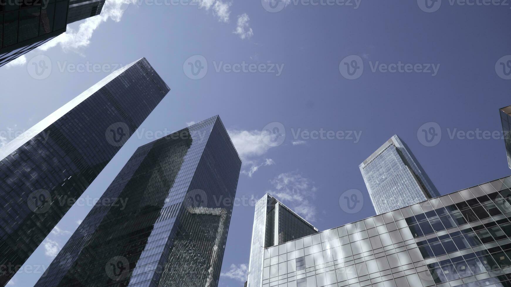 parte inferiore Visualizza di cime di bicchiere grattacieli su sfondo blu cielo. azione. moderno architettura di attività commerciale centri riflettendo blu cielo. vertiginoso Visualizza di moderno bicchiere grattacieli foto