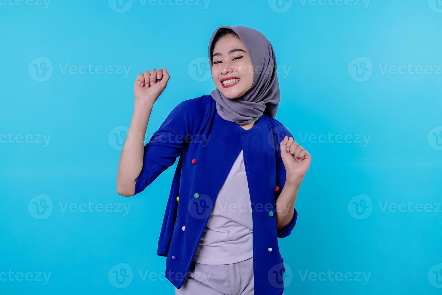 allegra giovane donna ha un'espressione positiva, stringe i pugni, ha un aspetto felicissimo, è di buon umore, indossa l'hijab, isolata sul muro blu foto