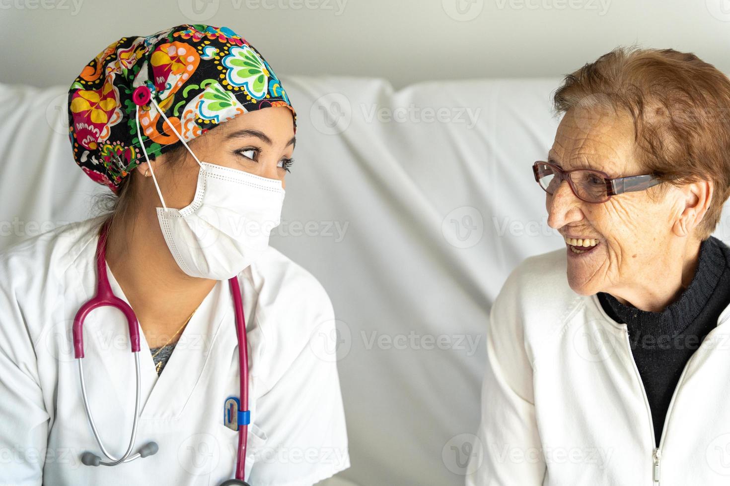 medico allegro in maschera che parla con donna anziana foto