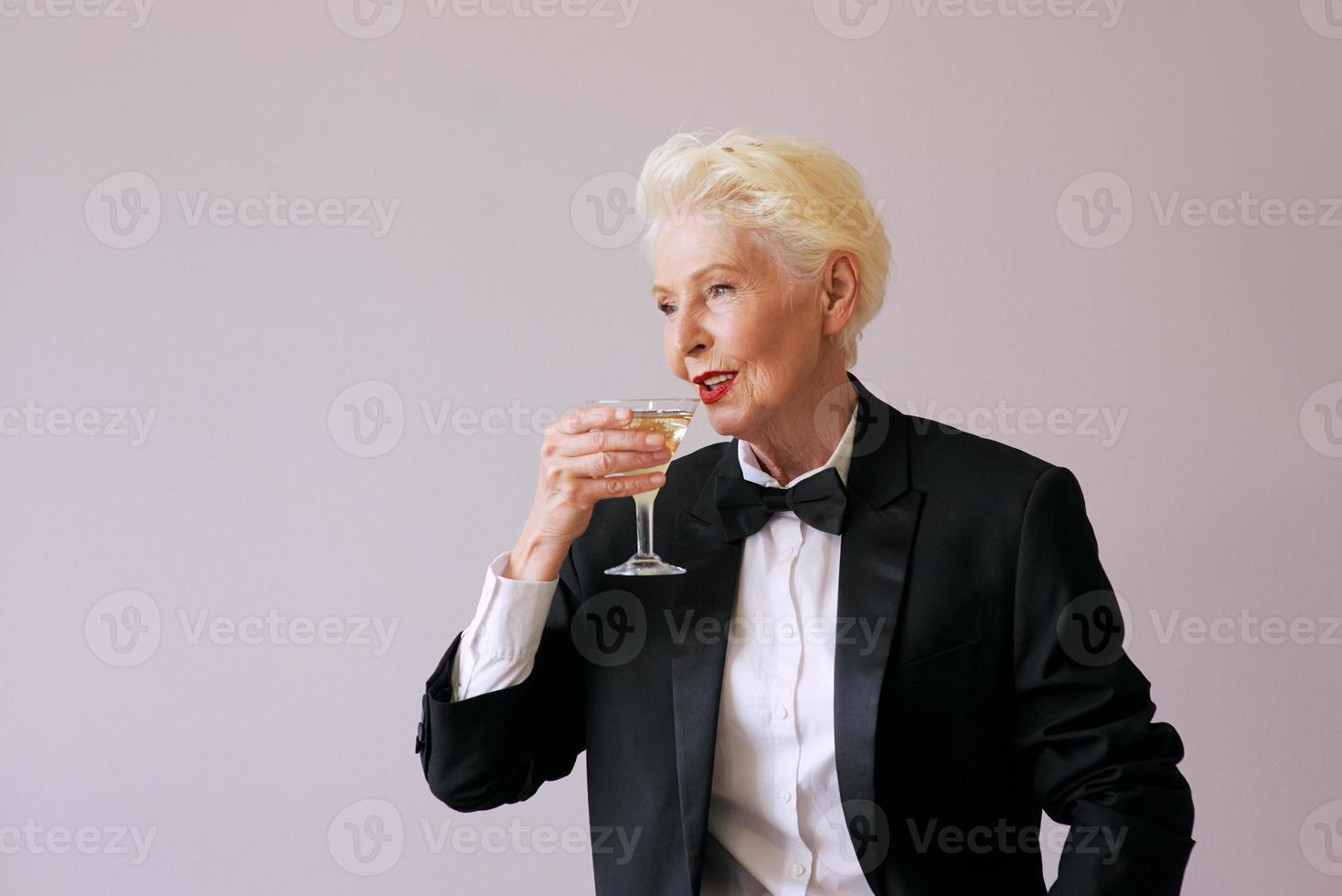 elegante maturo sommelier donna anziana in smoking con un bicchiere di spumante. divertimento, festa, stile, stile di vita, alcol, concetto di celebrazione foto