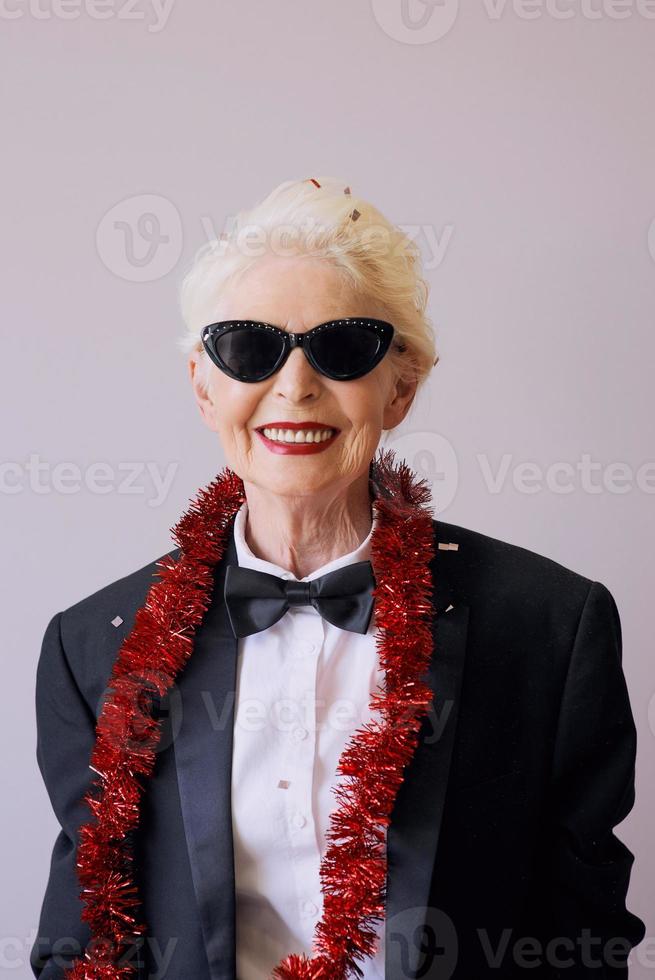 bella ed elegante donna anziana matura in occhiali da sole e smoking per celebrare il nuovo anno. divertimento, festa, stile, concetto di celebrazione foto