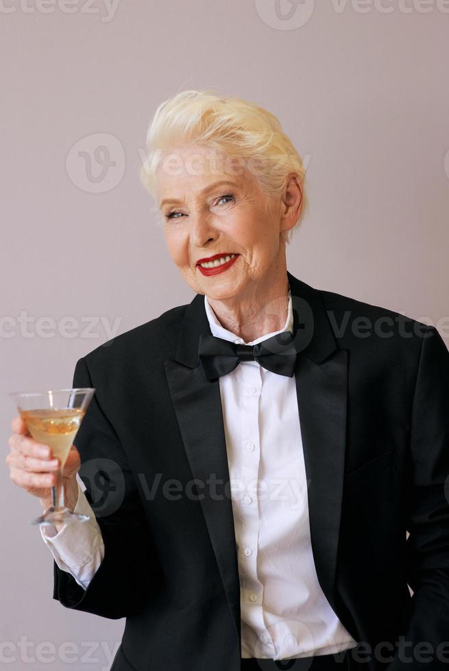 elegante maturo sommelier donna anziana in smoking con un bicchiere di spumante. divertimento, festa, stile, stile di vita, alcol, concetto di celebrazione foto