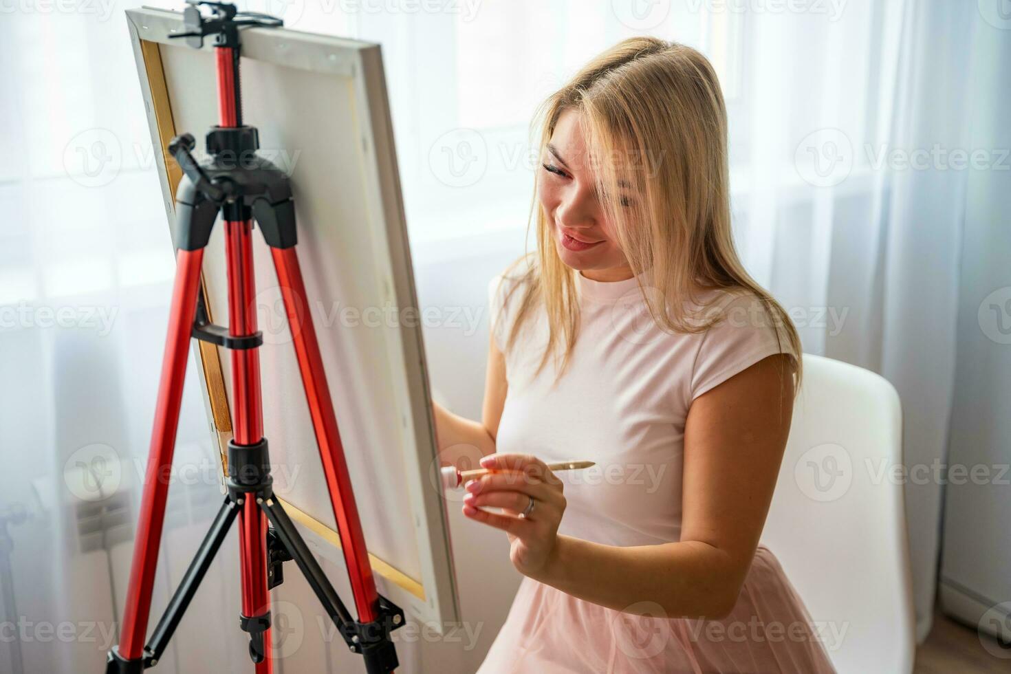 giovane donna artista con tavolozza e spazzola seduta e pittura immagine su tela vicino finestra. arte e creatività concetto. alto qualità foto