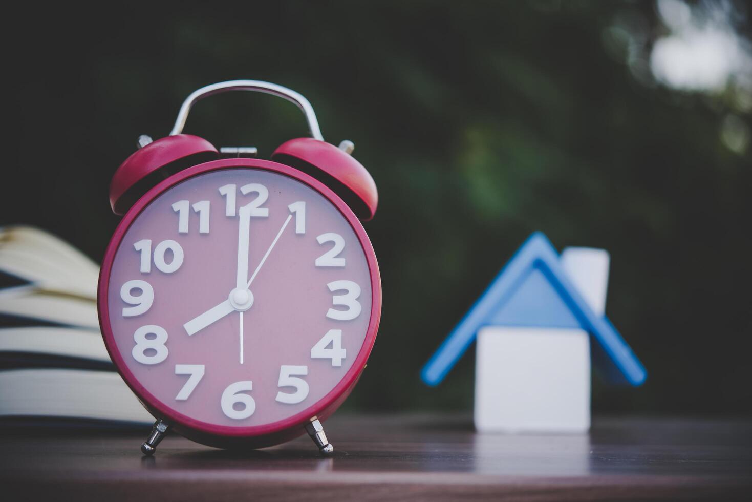 sveglia e modello di casa e libri sul tavolo di legno con sfondo bokeh. foto