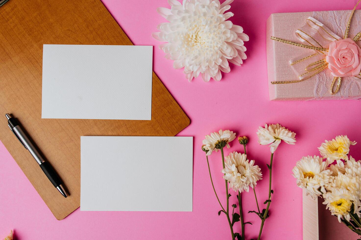 scatola regalo rosa, fiore, penna, tavola di legno e carta bianca su sfondo rosa foto