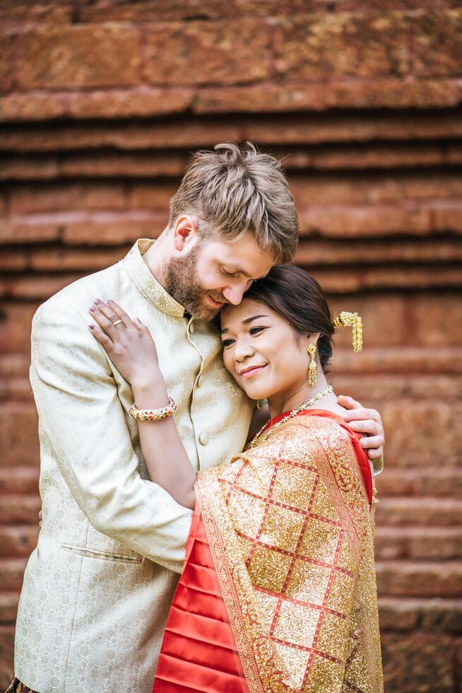 la sposa asiatica e lo sposo caucasico hanno un momento romantico con il vestito thailandese foto