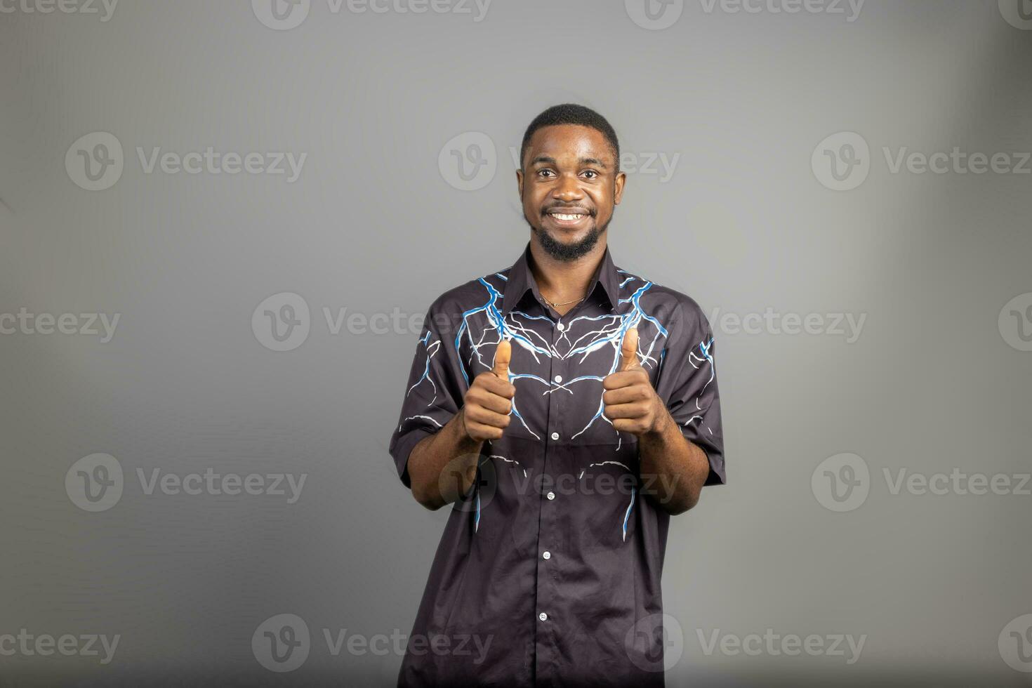 giovane uomo sorridente a grandi linee guardare felice, positivo, fiducioso e riuscito, con tutti e due pollici su foto