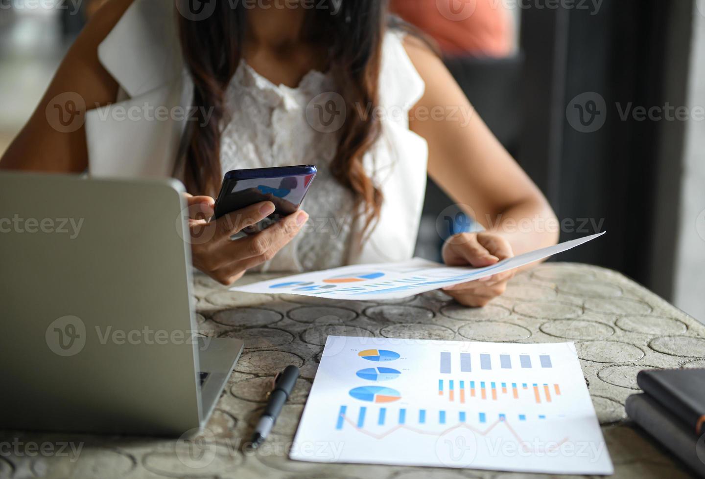 le dirigenti donne usano i telefoni cellulari e controllano i grafici dei dati. laptop, grafici e penna posto sulla scrivania. foto