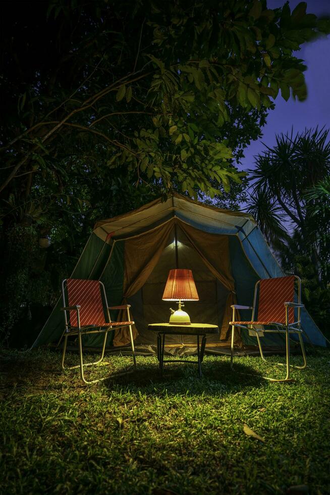 Vintage ▾ cabina tenda, antico olio lampada su un' di legno tavolo con retrò sedie. a notte nel il foresta foto