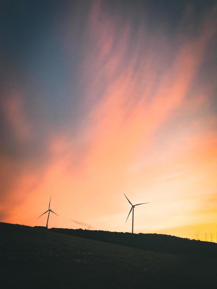 sagome di turbine eoliche nel campo vista aerea tramonto arancione brillante cielo blu vento parco rallentatore drone girare. mulini a vento di sagome, grande cielo arancione drammatico con nuvole. energia sostenibile foto