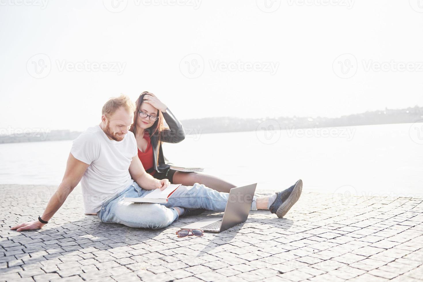 due studenti, ragazzo e ragazza, sono seduti all'aperto e si godono un laptop, studiando all'aperto in una giornata di sole foto