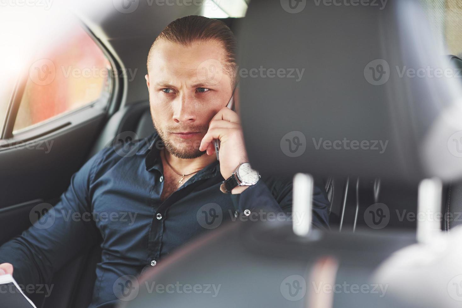 un uomo d'affari che invia un messaggio a uno smartphone e si avvicina al sedile posteriore dell'auto. foto