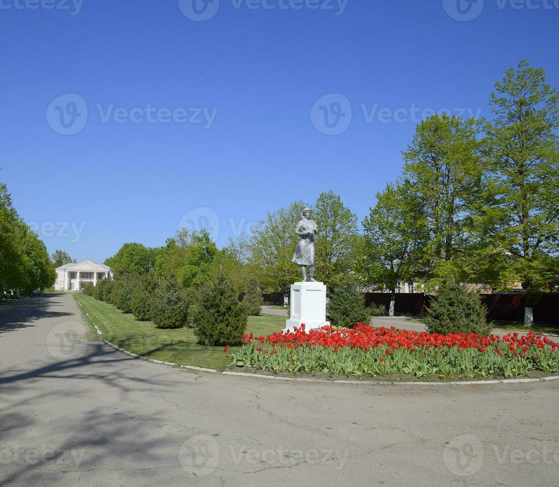 statua di un' collettivo contadino su un' piedistallo. il eredità di il sovietico era. un' fiore letto con tulipani e giovane alberi nel il villaggio di oktyabrsky. krasnodar Krai, Krasnoarmeisky quartiere. foto