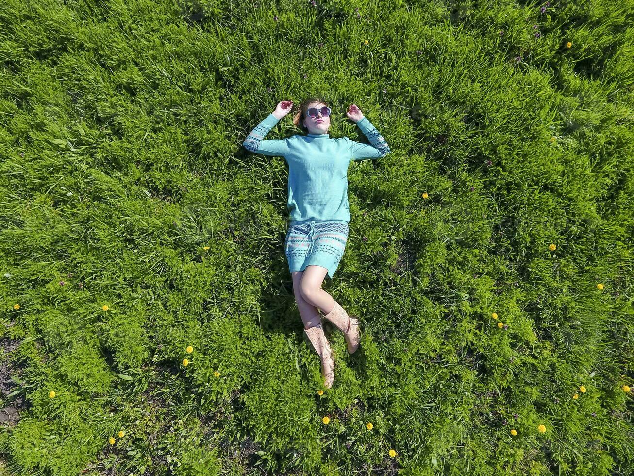 il ragazza bugie nel un' turchese vestito su il prato. bellissimo ragazza dire bugie giù di erba foto